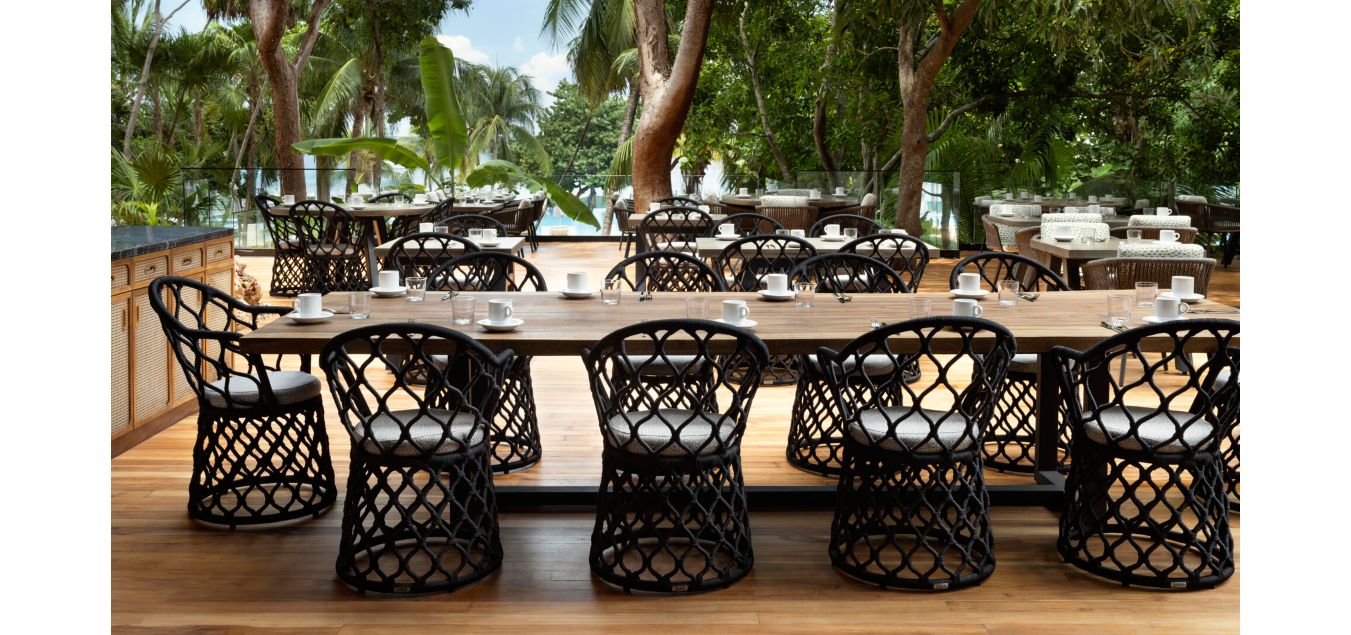 户外用餐区域位于木质露台，周围热带树木环绕，可眺望壮丽海景