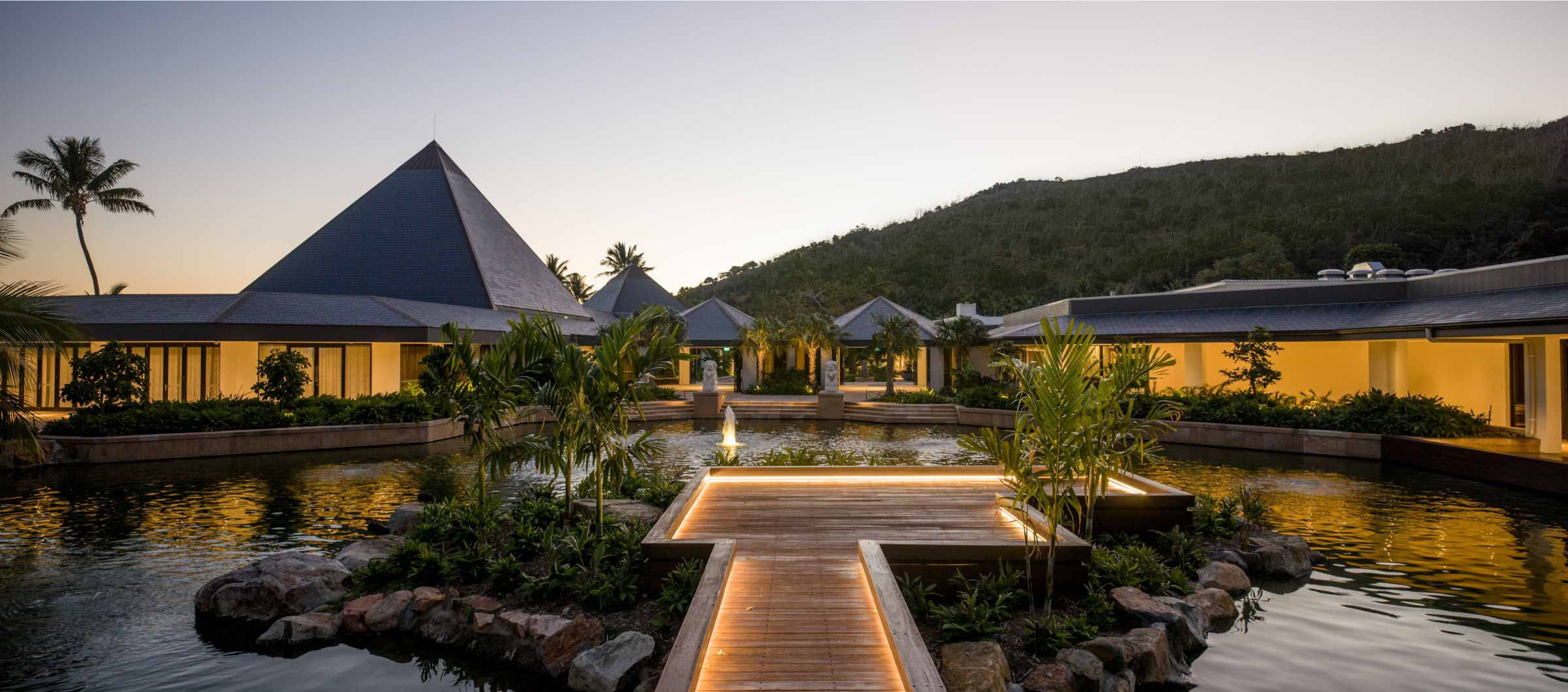Lit walkway extending out into the middle of a pond surrounded by the hotel