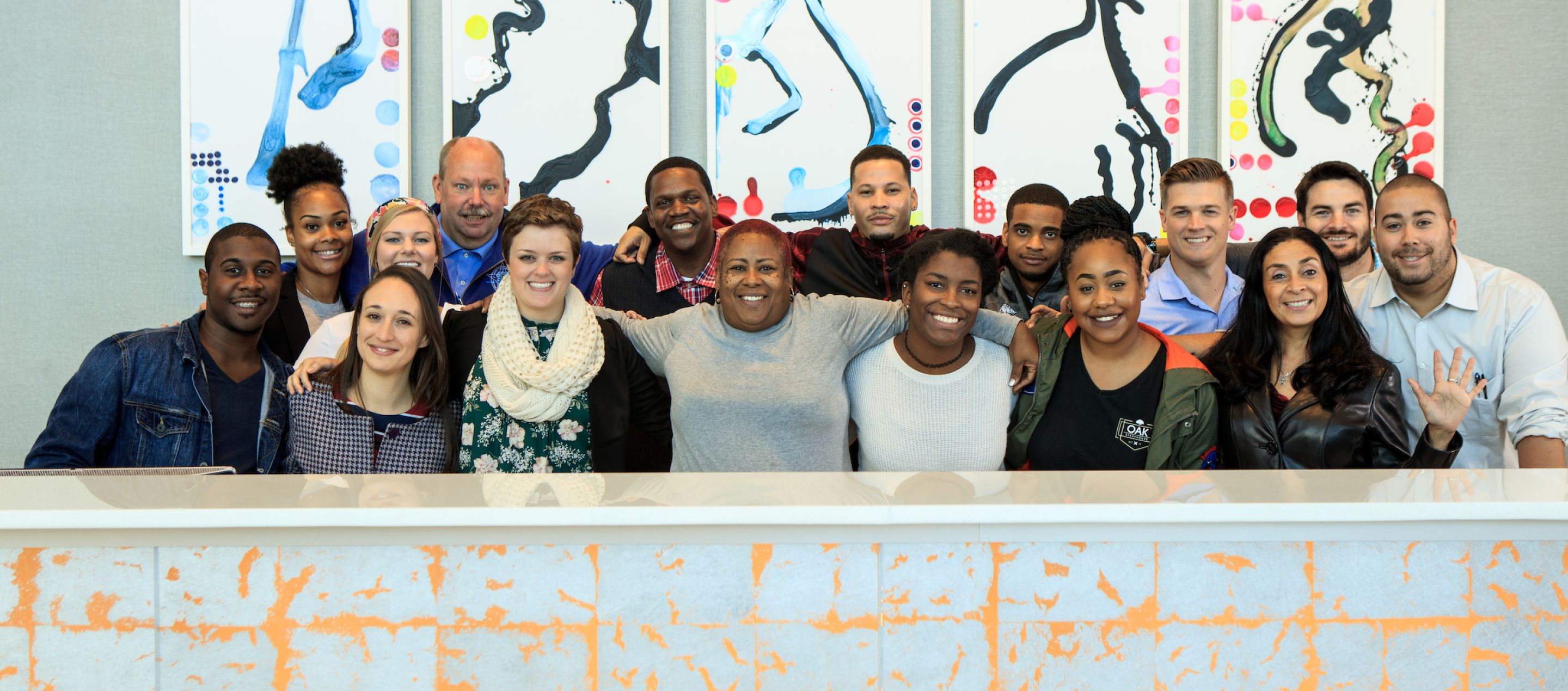 sixteen people standing in front of colorful simplistic artwork