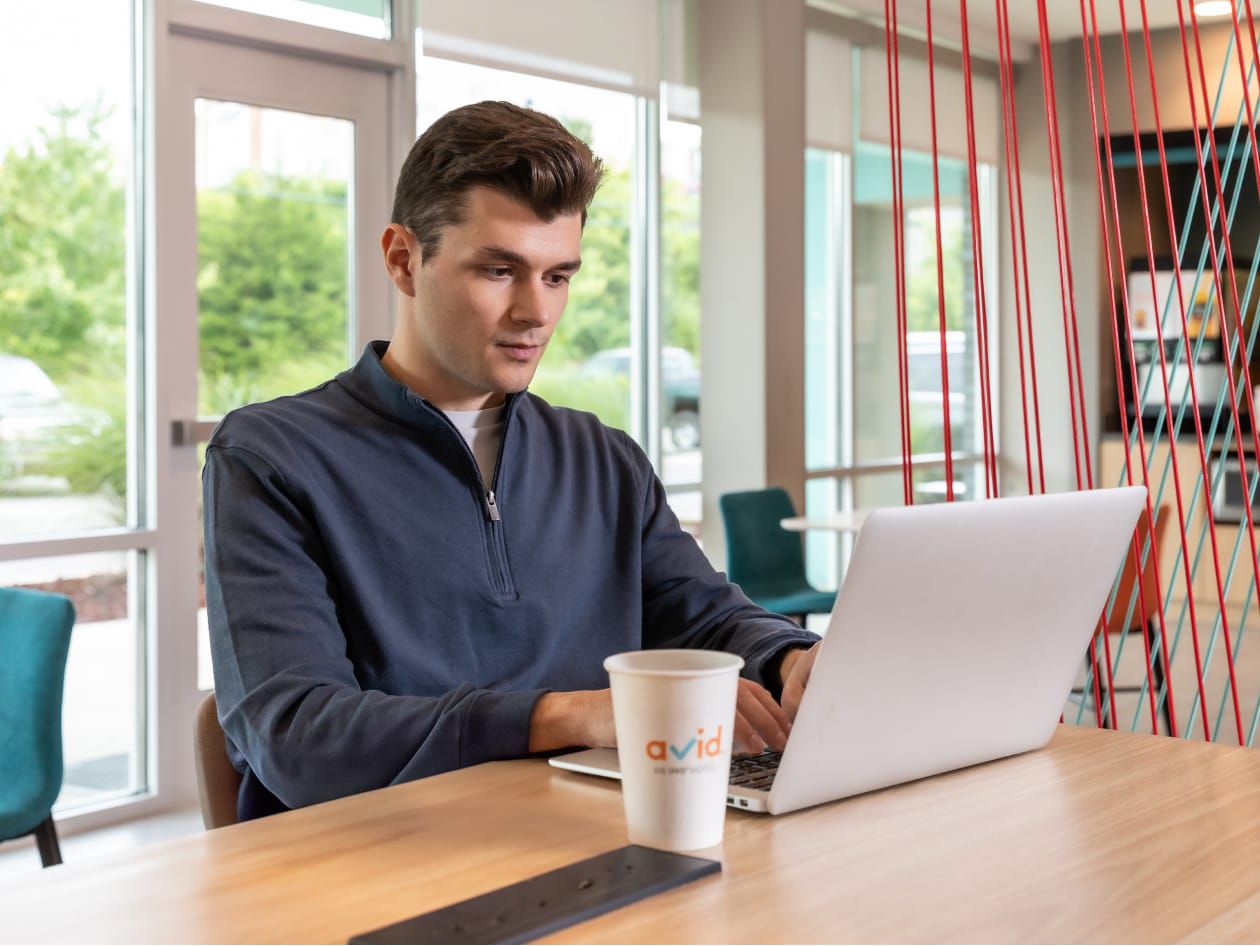 Man working on his laptop at a breakfast table with an avid coffee cup