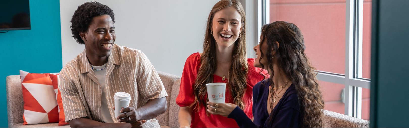 Three friends sitting on a couch drinking fresh coffee from avid to-go cups