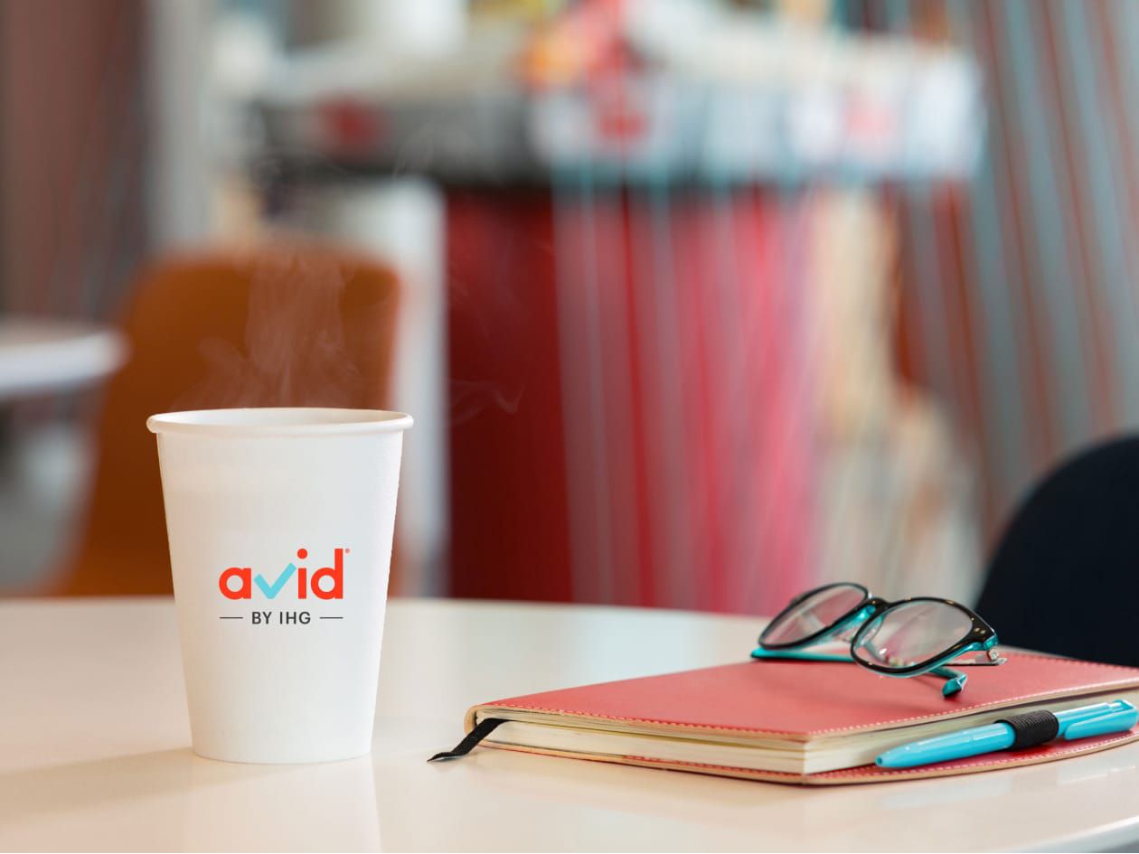 Coffee cup with avid logo, notebook and glasses lying on table