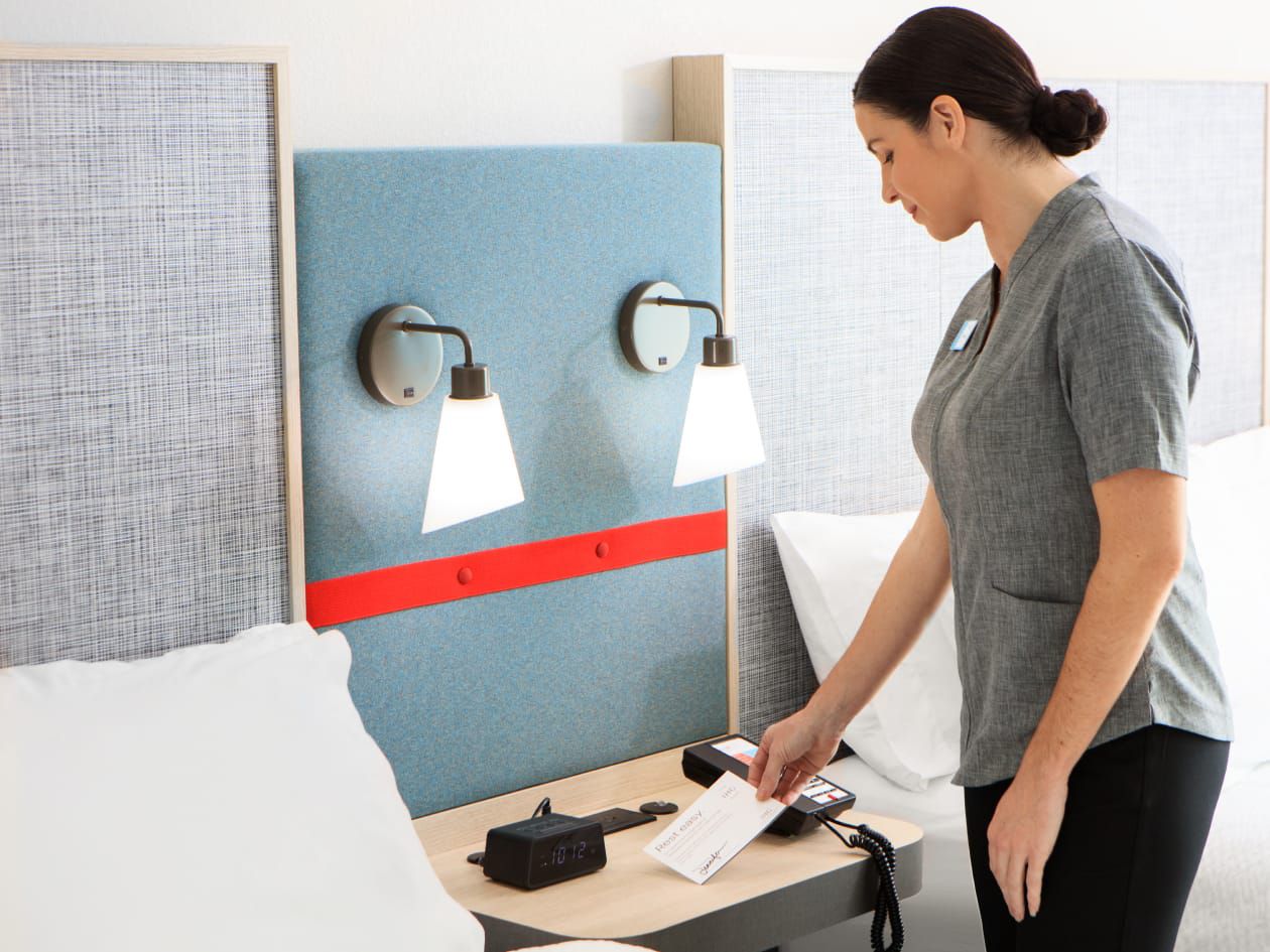 Housekeeper placing card on bedside table in clean hotel room