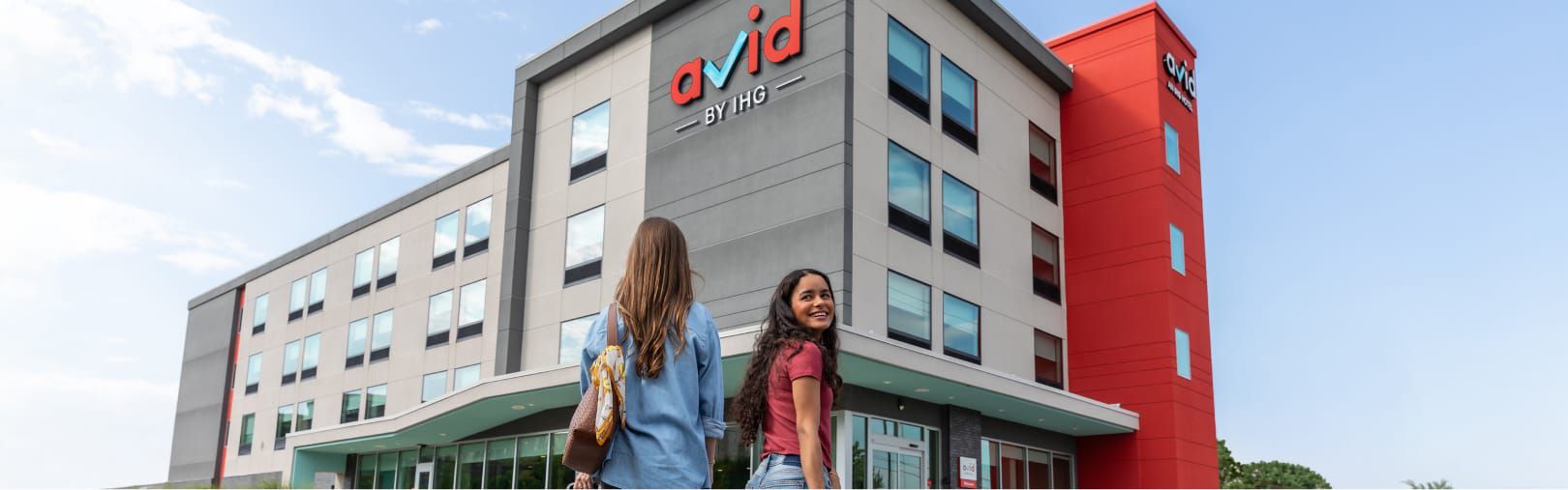Two women walking up to an avid hotel with their suitcases