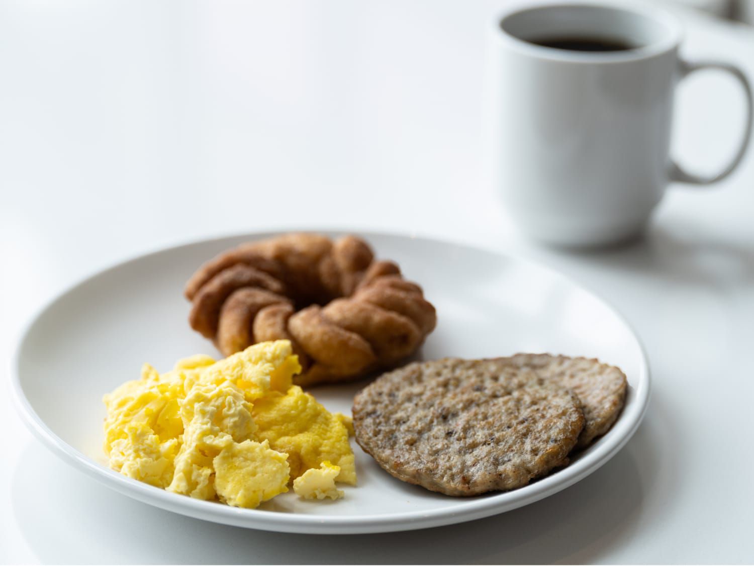 A breakfast plate with scrambled eggs, a doughnut and sausage patties.