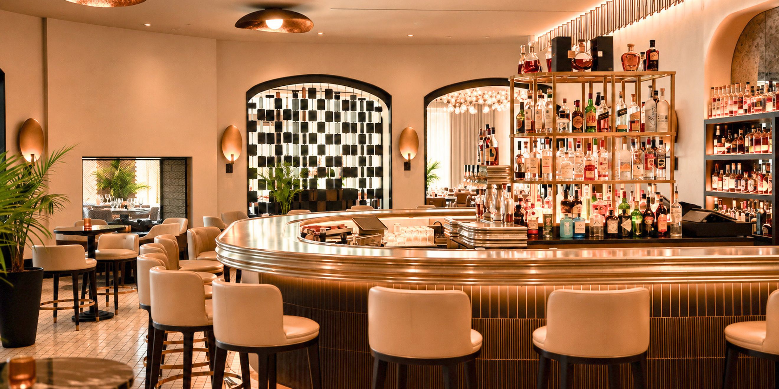 Elegant hotel bar featuring a curved illuminated counter, upholstered bar seating, and shelves stocked with premium spirits in a warm, contemporary
