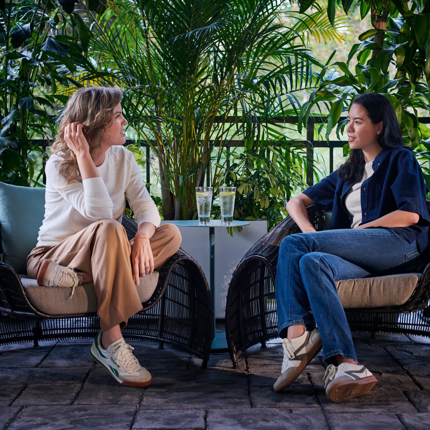Two women conversing on a patio surrounded by greenery.