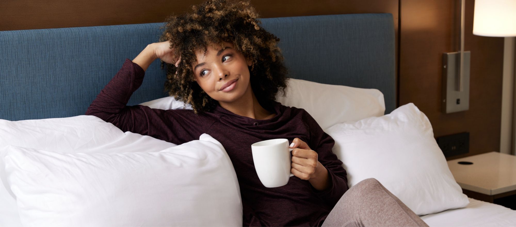 woman lounging on hotel bed with mug