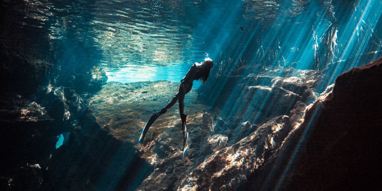Underwater image of woman swimming in rocky sunlit waters