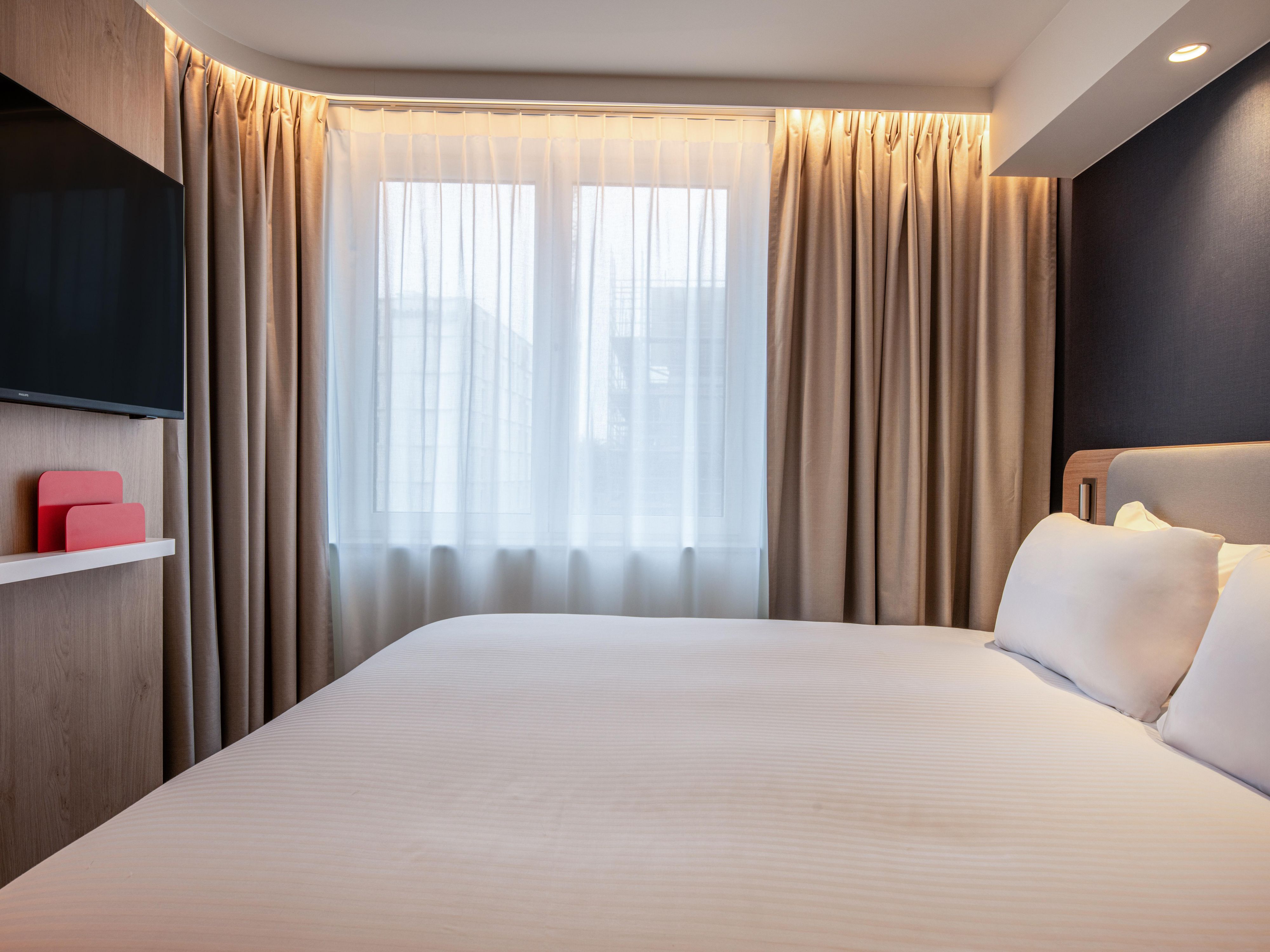 hotel guest bedroom with king sized bed, and large window, offering natural lighting