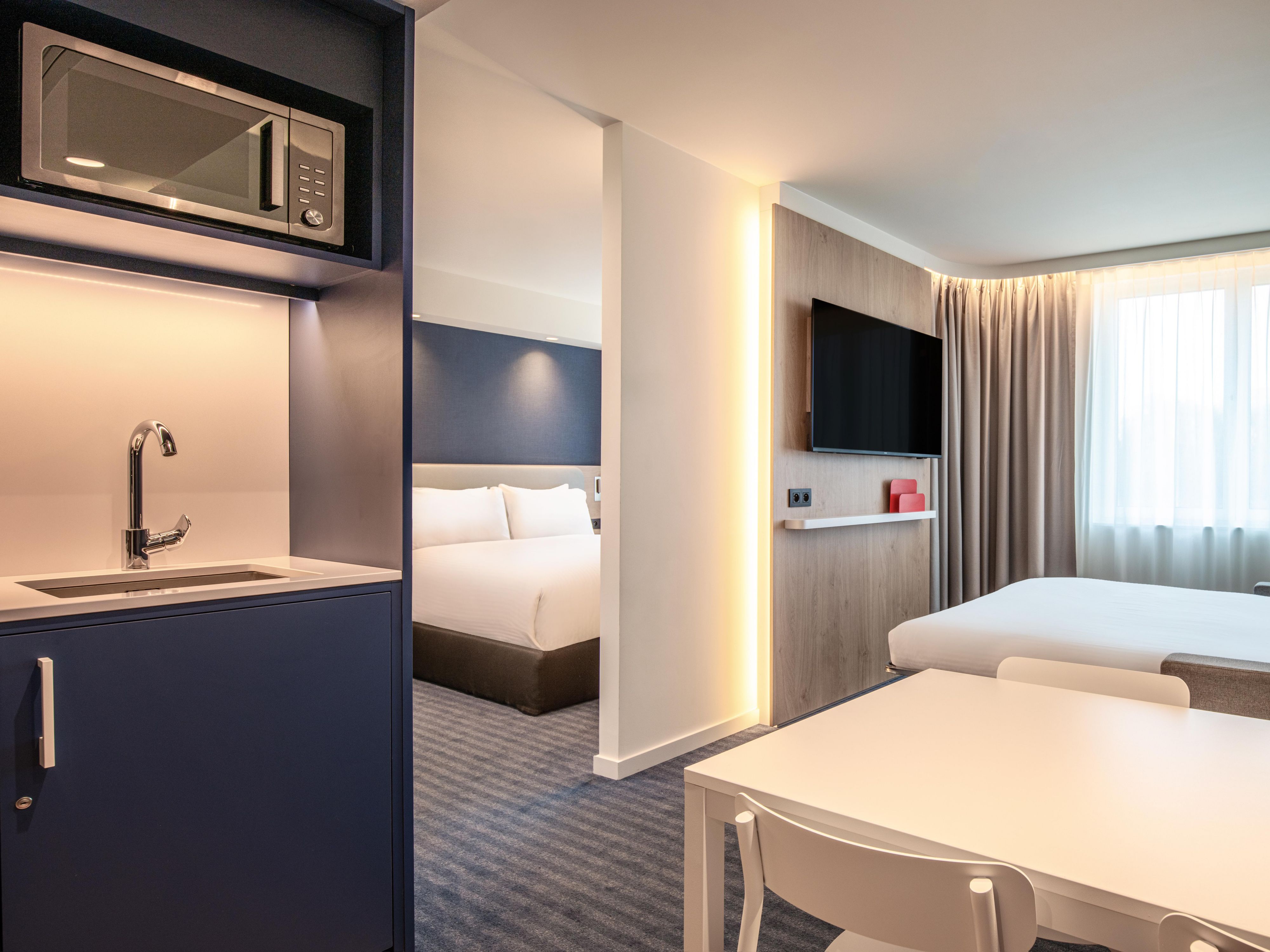 hotel guest suite with kitchenette, sofa bed, dining table and natural lighting