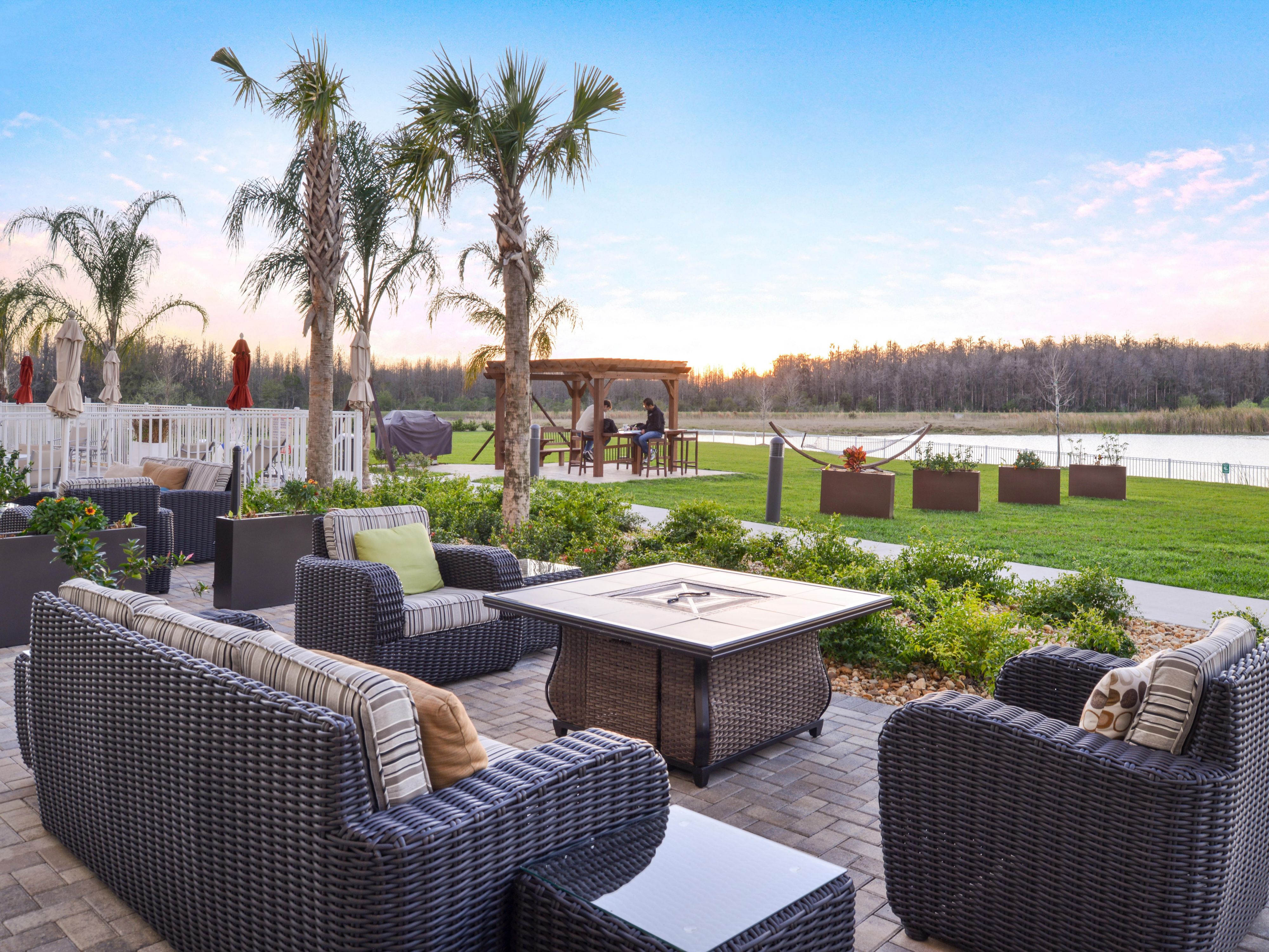 Guests enjoy a heated outdoor pool and hot tub set next to a tropical sundeck with fire pit,  grill, hammocks, and corn hole.