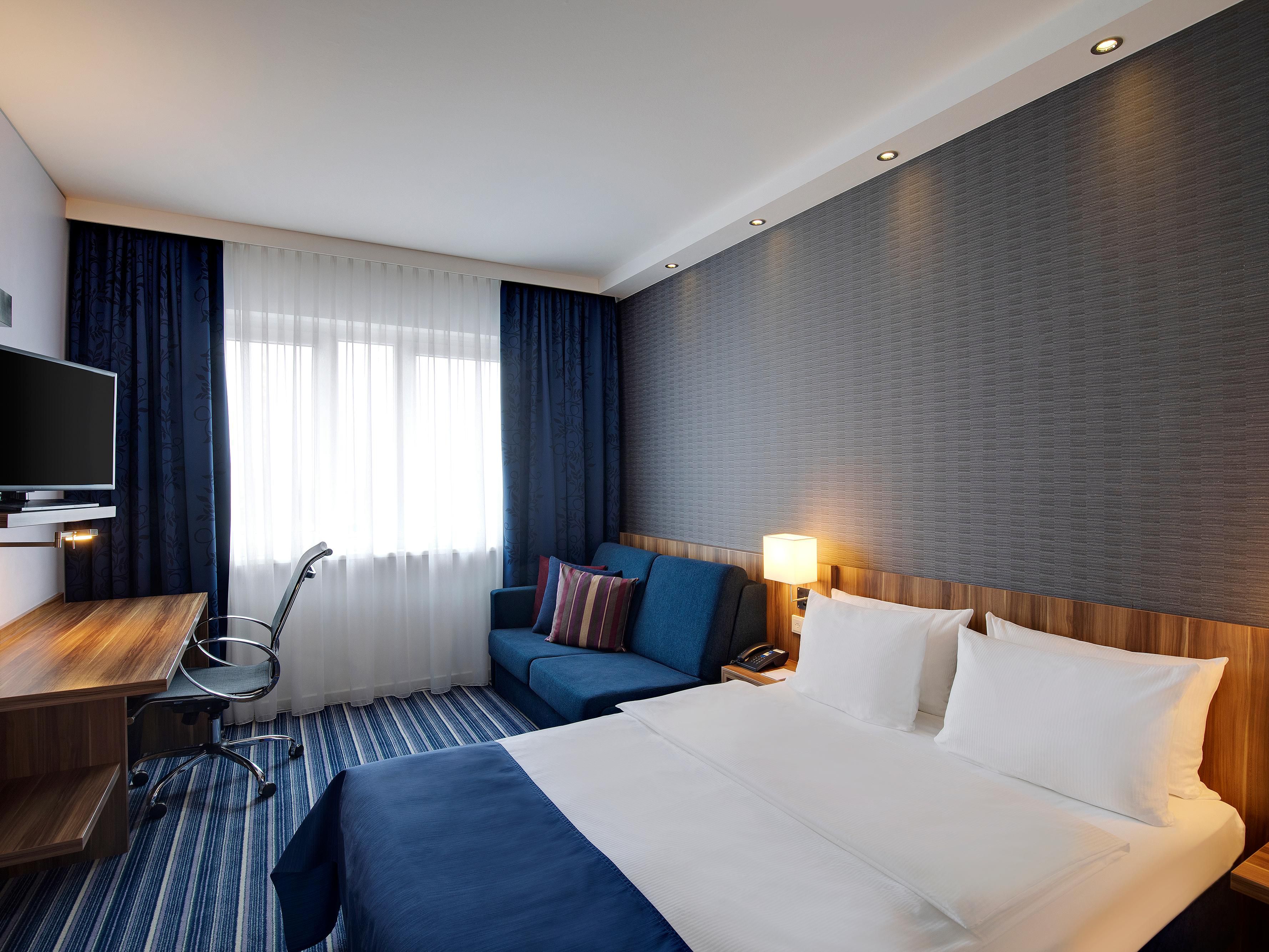 A spacious room with a double bed, sofa and executive desk.
