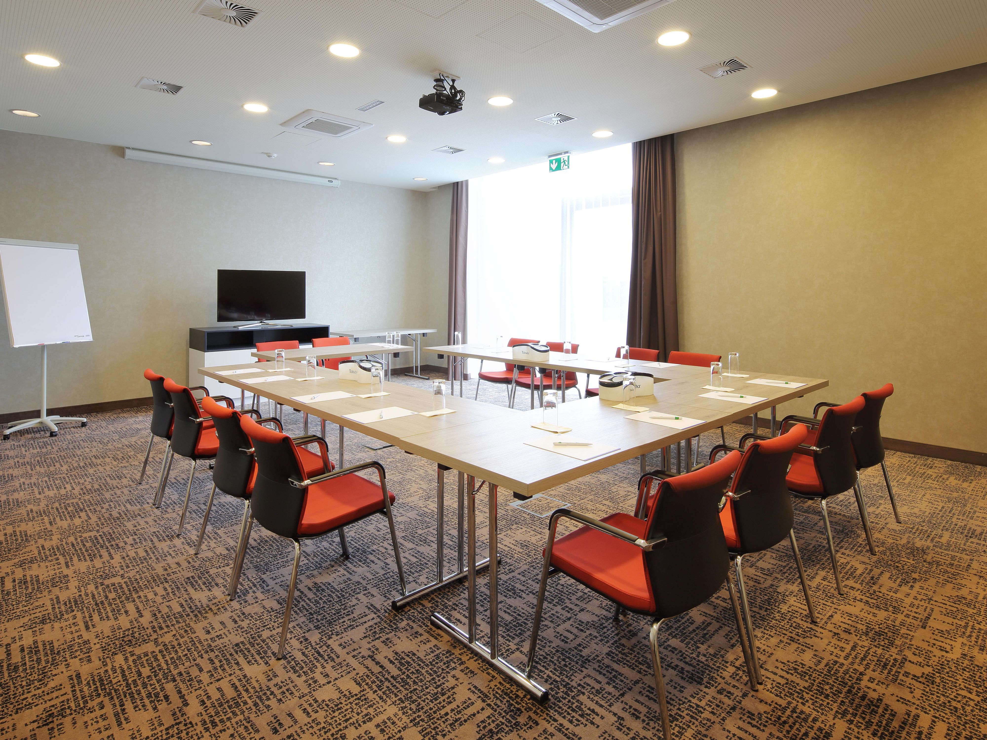 We offer a modern meeting room of 64 sqm, which can be divided into two separate rooms of 32 sqm each with a partition wall. The rooms are bright, air-conditioned, and equipped with modern technology. A projector, screen, flipchart, and pinboards are available. The light-flooded atmosphere provides a pleasant environment for your meeting.