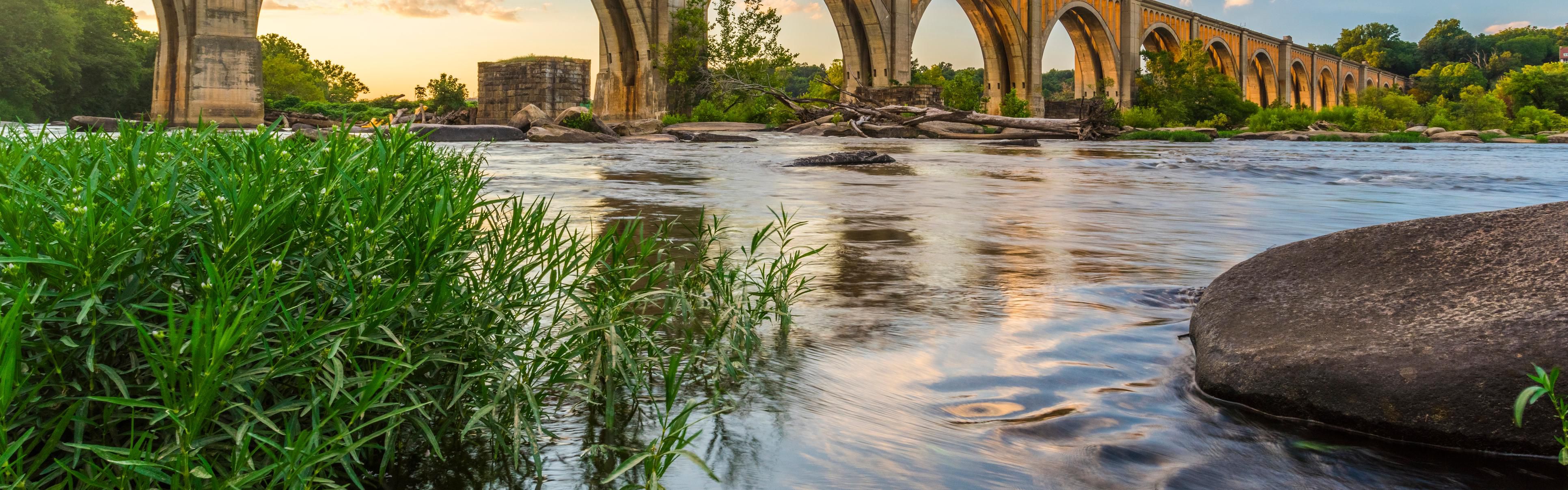 Arched concrete bridge spanning a calm river at sunset.