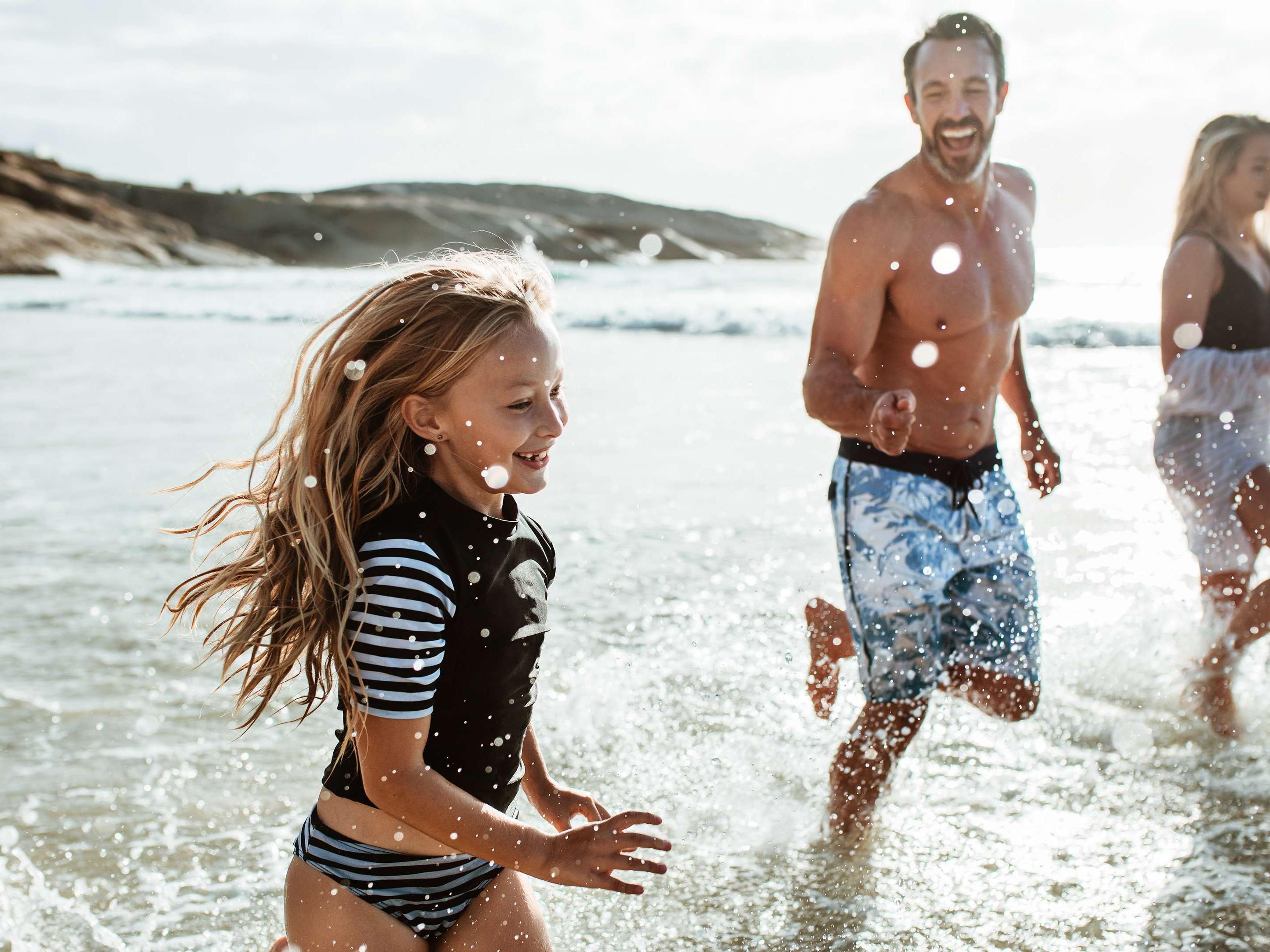 Girl running through the ocean waves with her dad