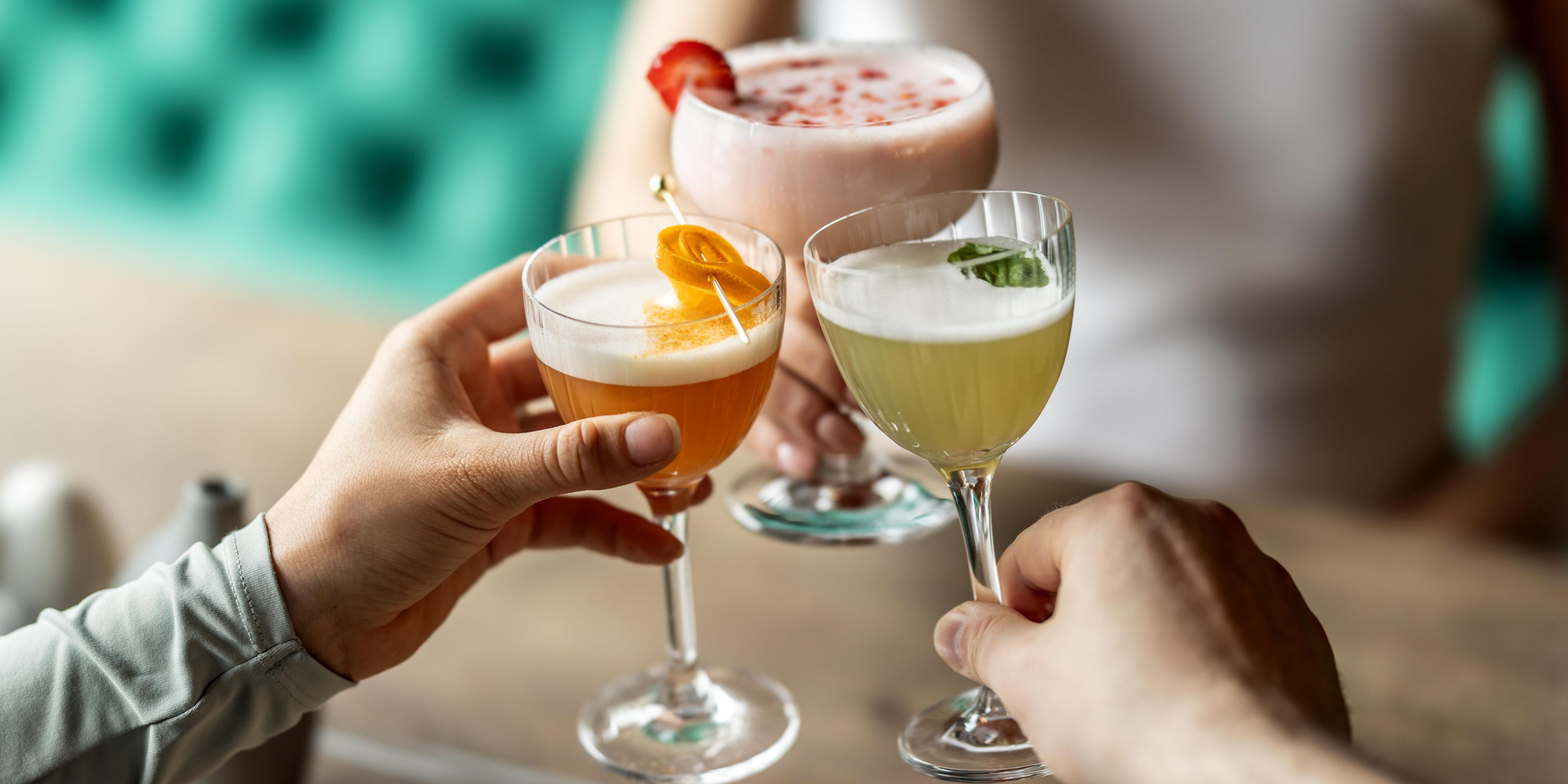 group of three cheersing with various colourful cocktails