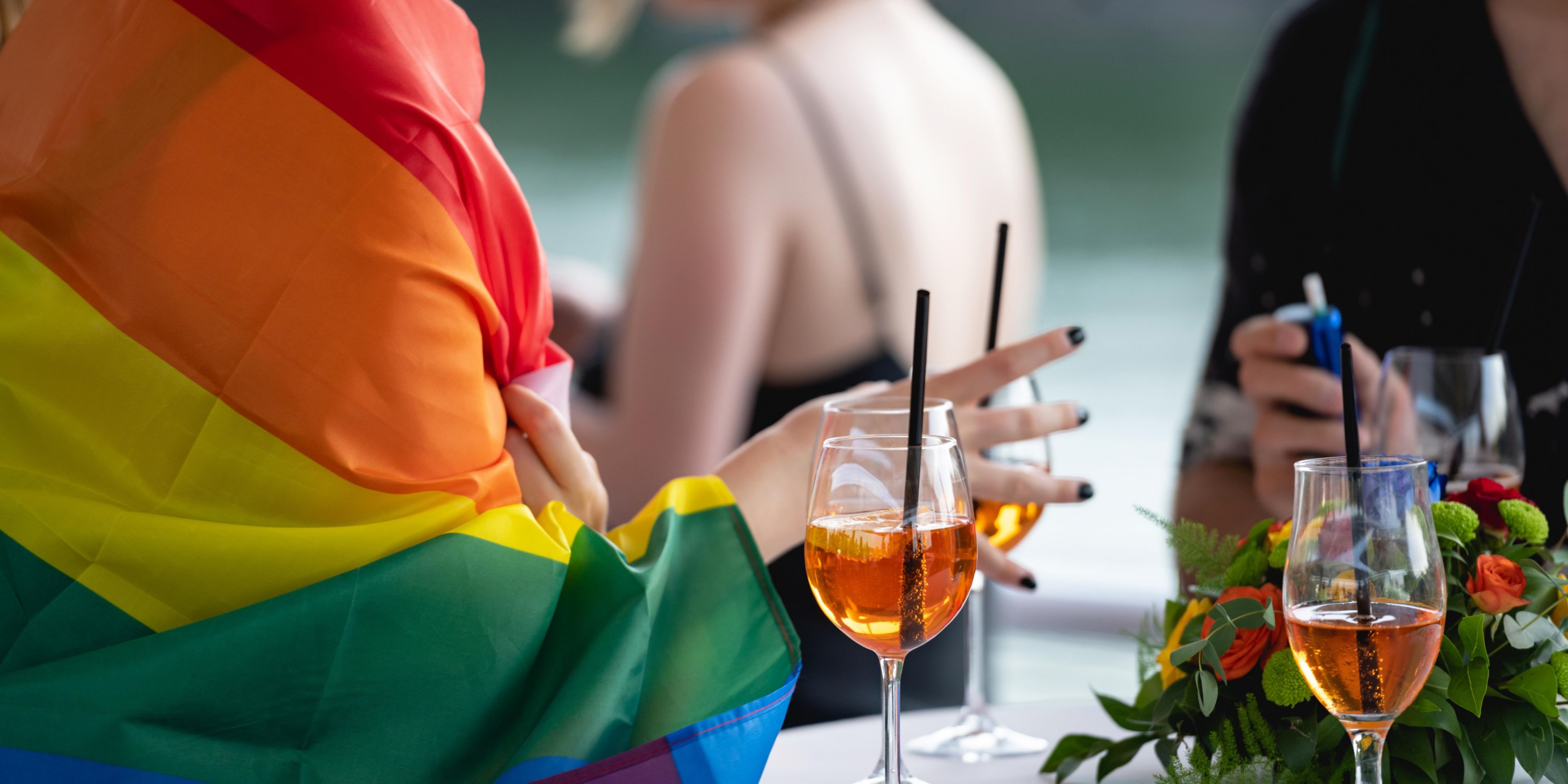 person with pride flag wrapped around them, sipping cocktails