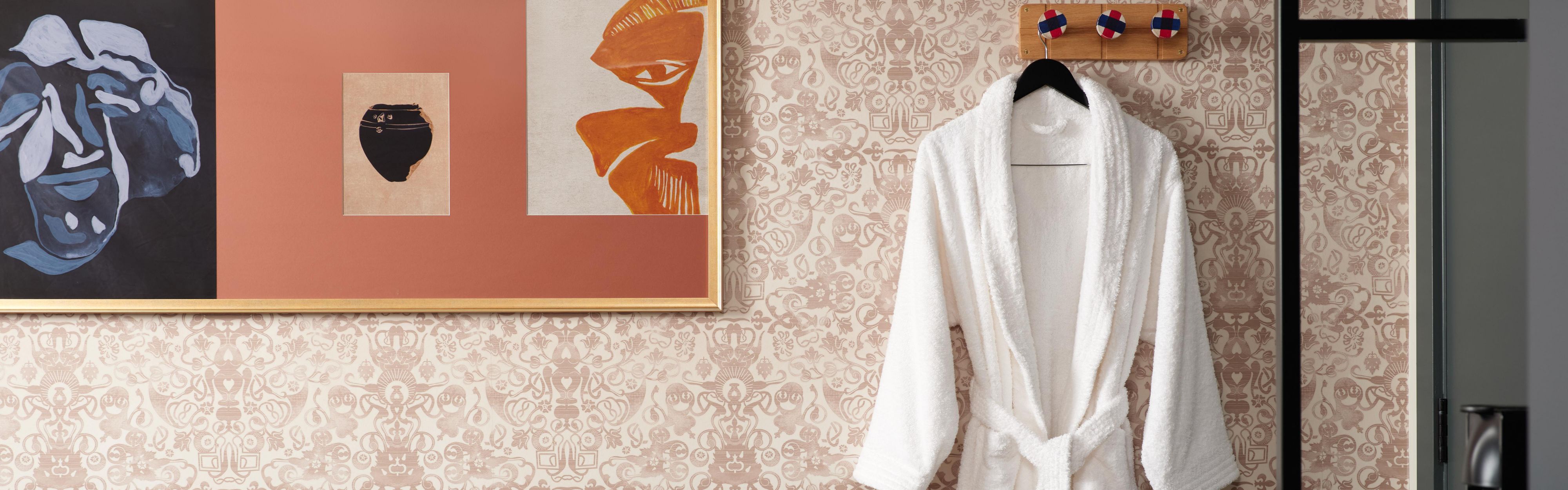 hotel guest room featuring a hanging white robe, printed wallpeper, sofa and wall prints
