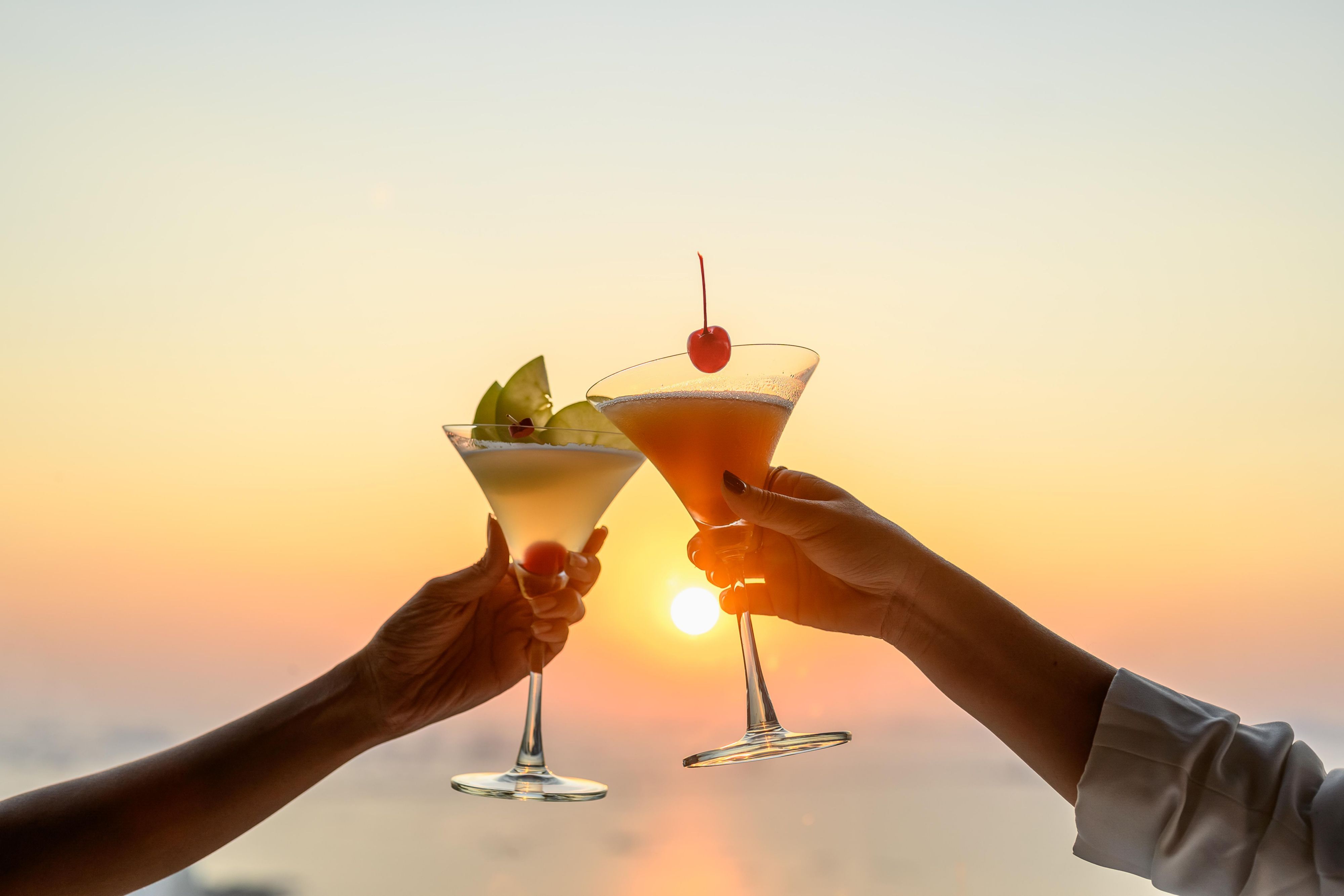 Two guests toasting with cocktails with a sunset view.
