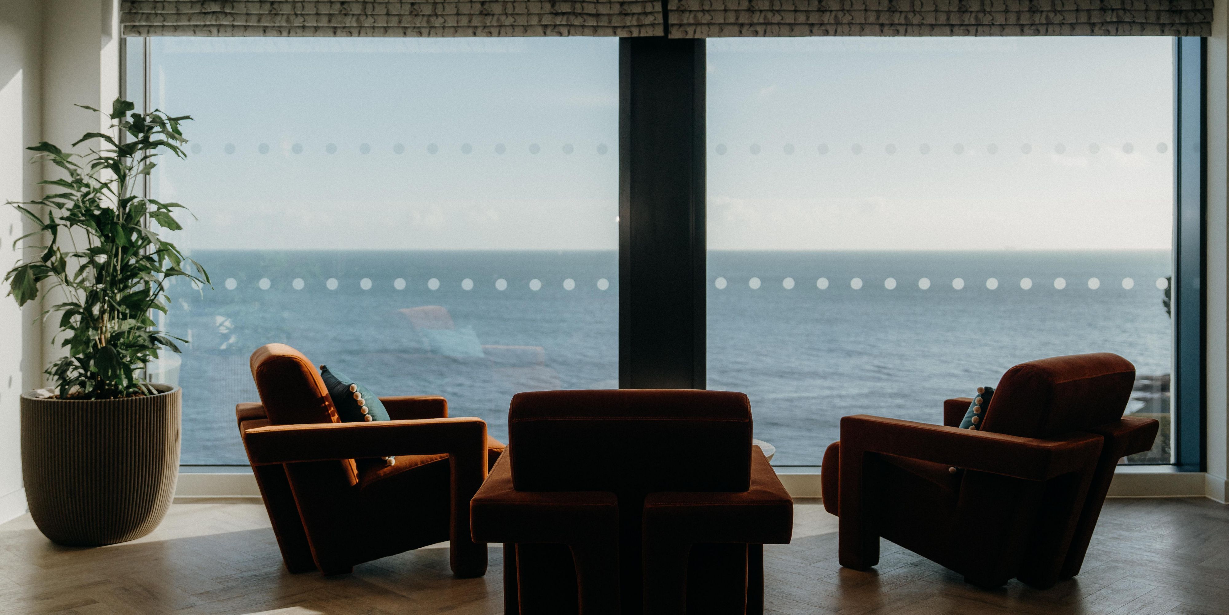 three large cosy armchairs, placed in front of a large window offering scenic views of the ocean