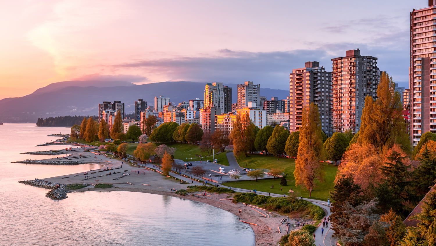 A quiet evening on the waterfront where the sun is setting beyond the buildings and mountains.