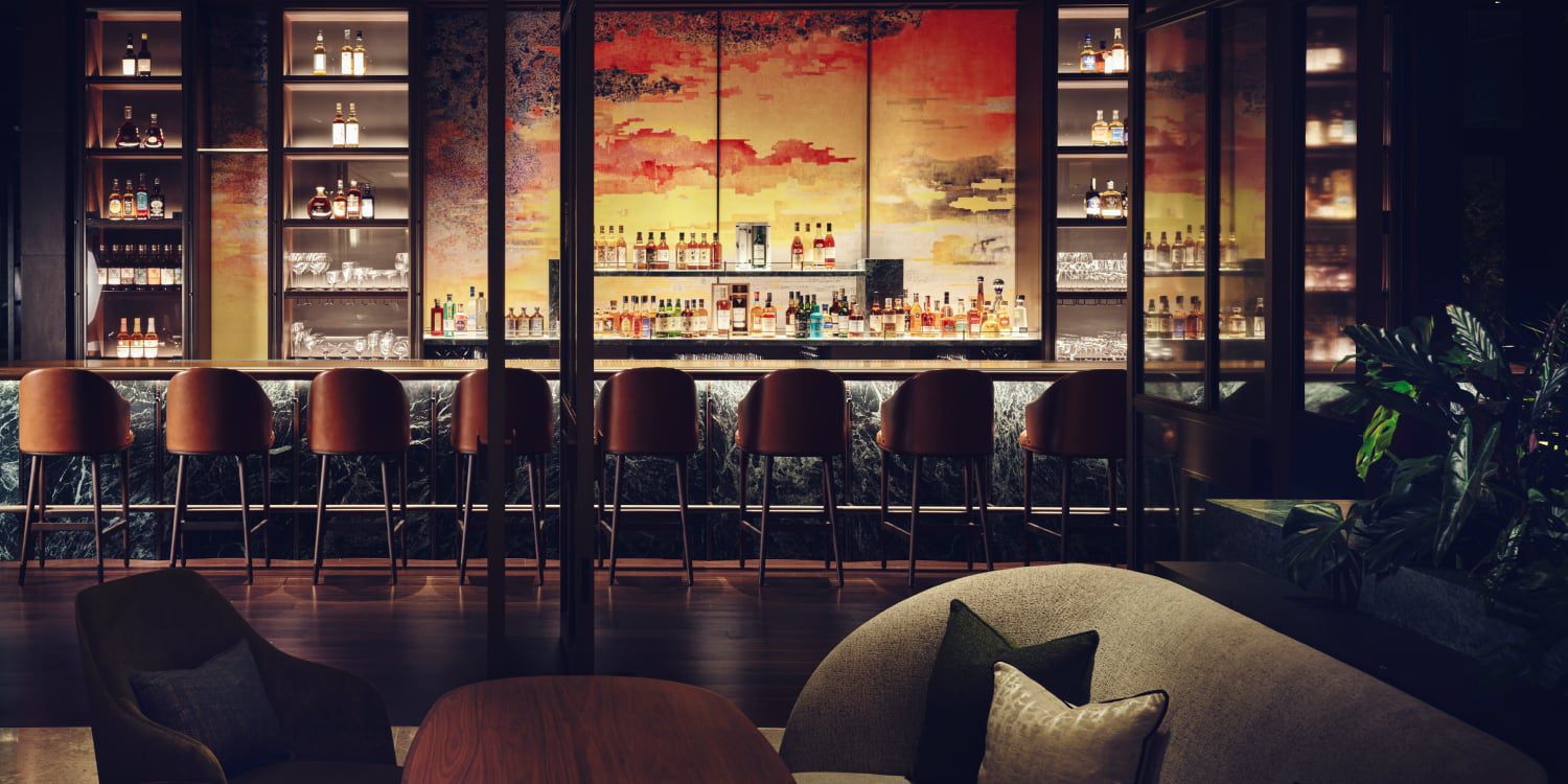 A fully stocked bar with a vibrant mural of reds, oranges and yellows as a backdrop.