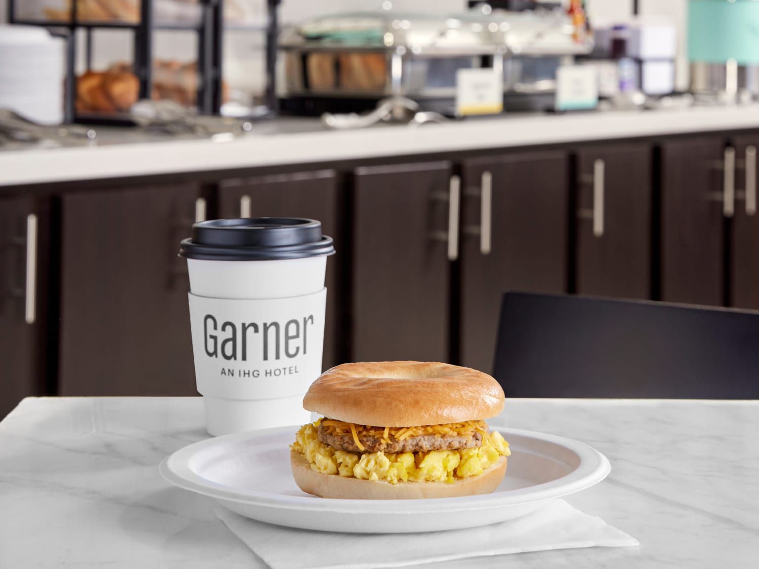 一份热腾腾的早餐三明治，配香肠和鸡蛋，外加一杯现磨咖啡，装在随行杯里。