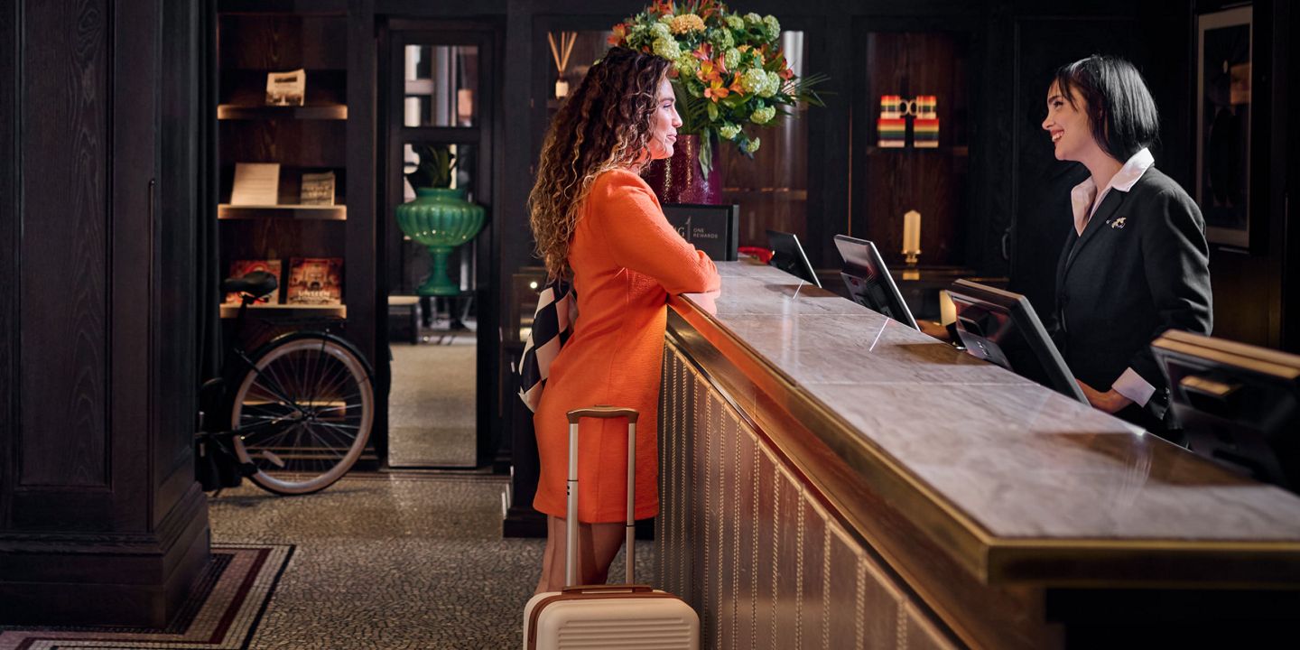 Hotel check-in at front desk with suitcase and flowers.
