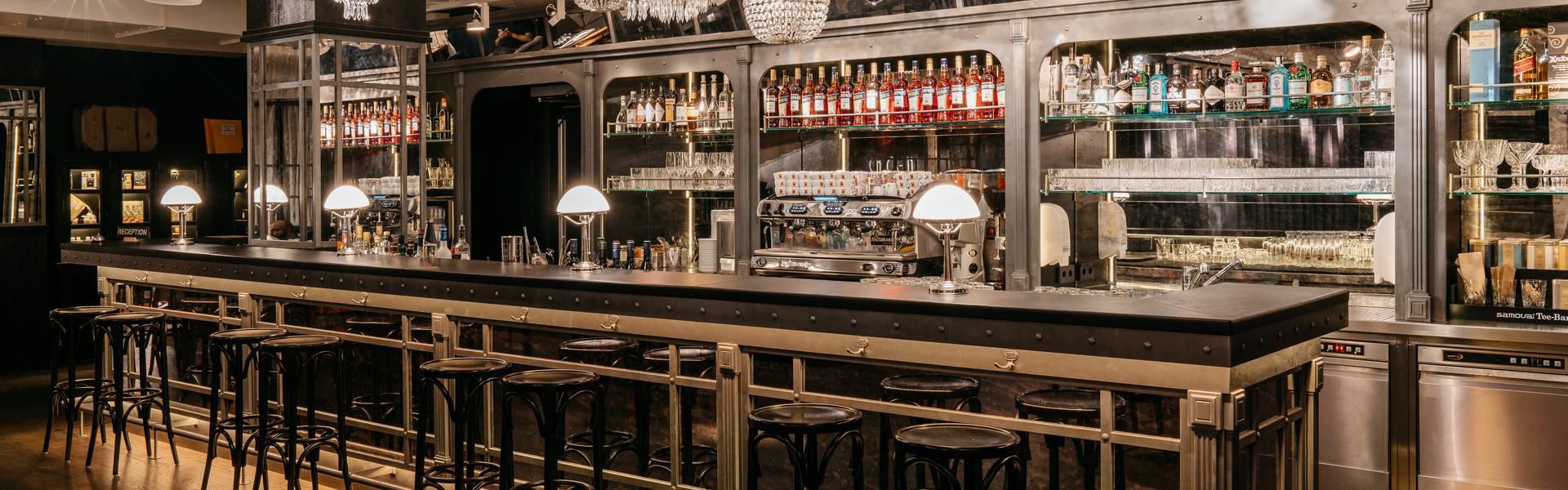 Elegant dimly lit hotel bar with classic decor, mirrored shelving, and a professional espresso machine.