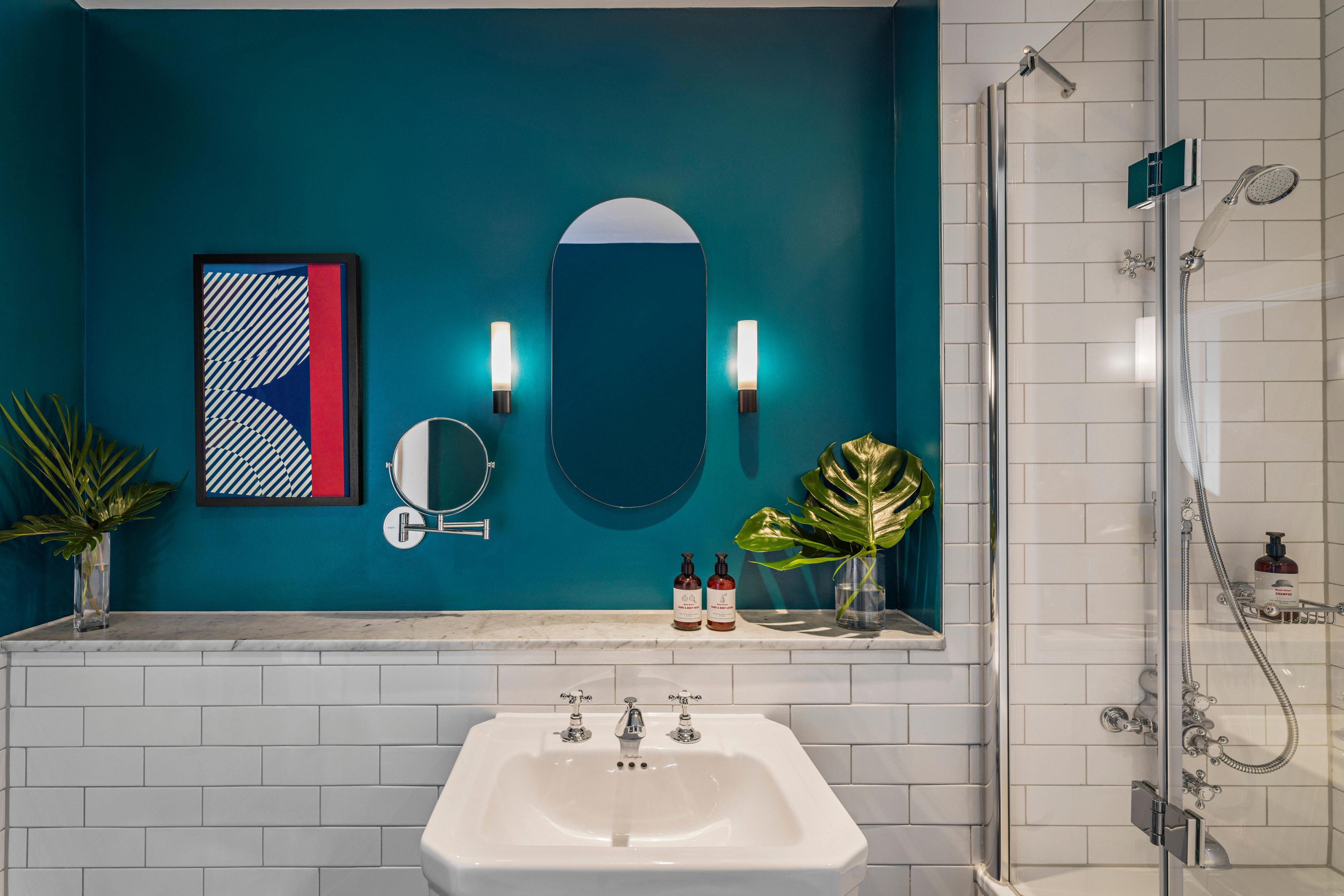 Blue hotel suite bathroom with sink, mirror, shower and added shower product amenities