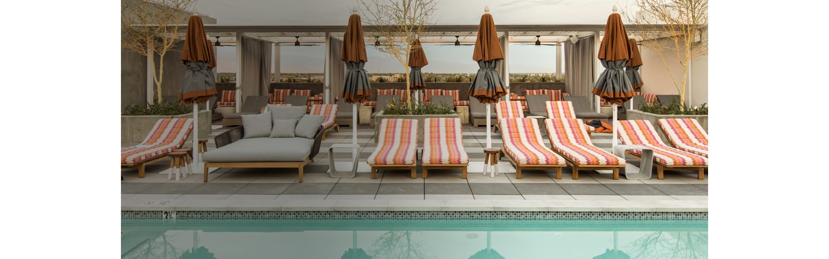striped chaise lounges line a pool with views of desert mountains behind