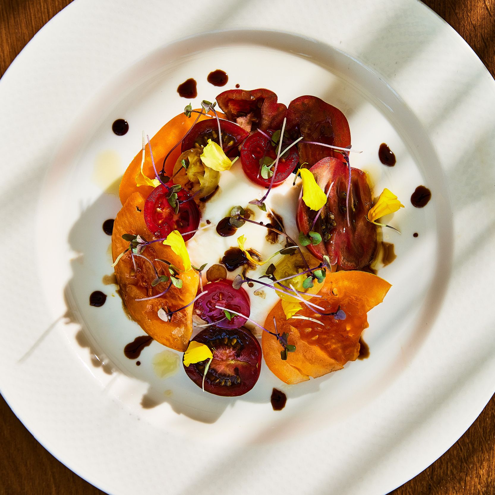 deeply coloured sliced tomatoes around burrata on a white plate
