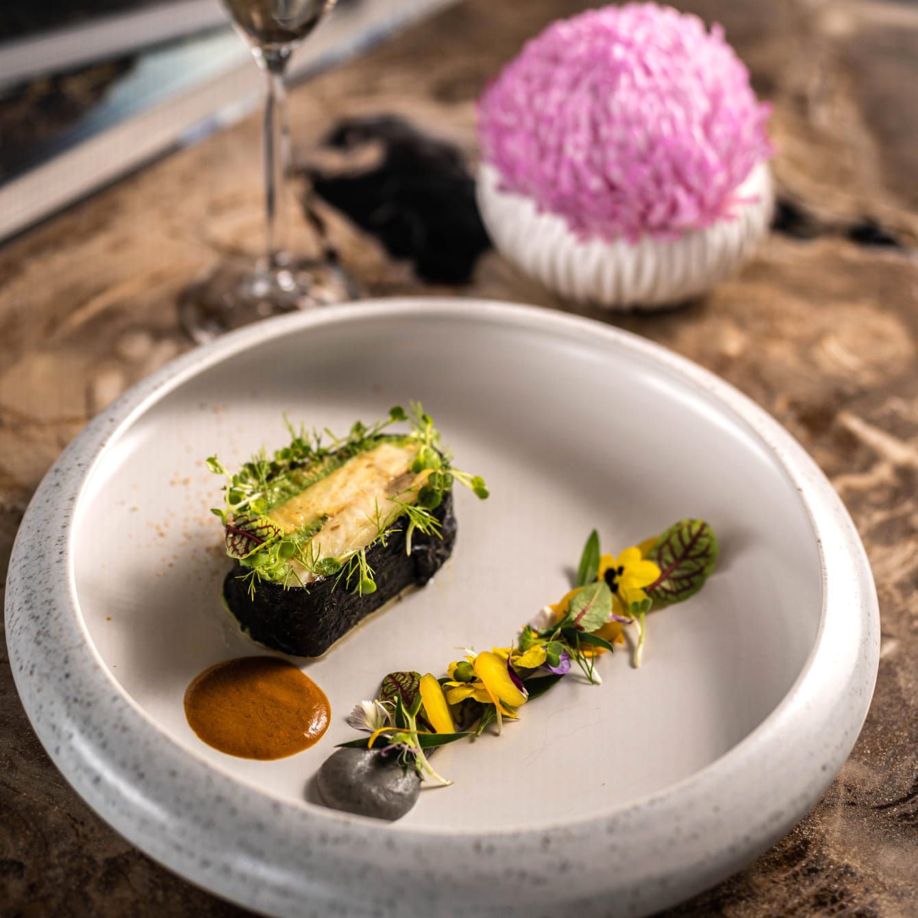 Seared fish plated elegantly with flowers and other edible garnishes.