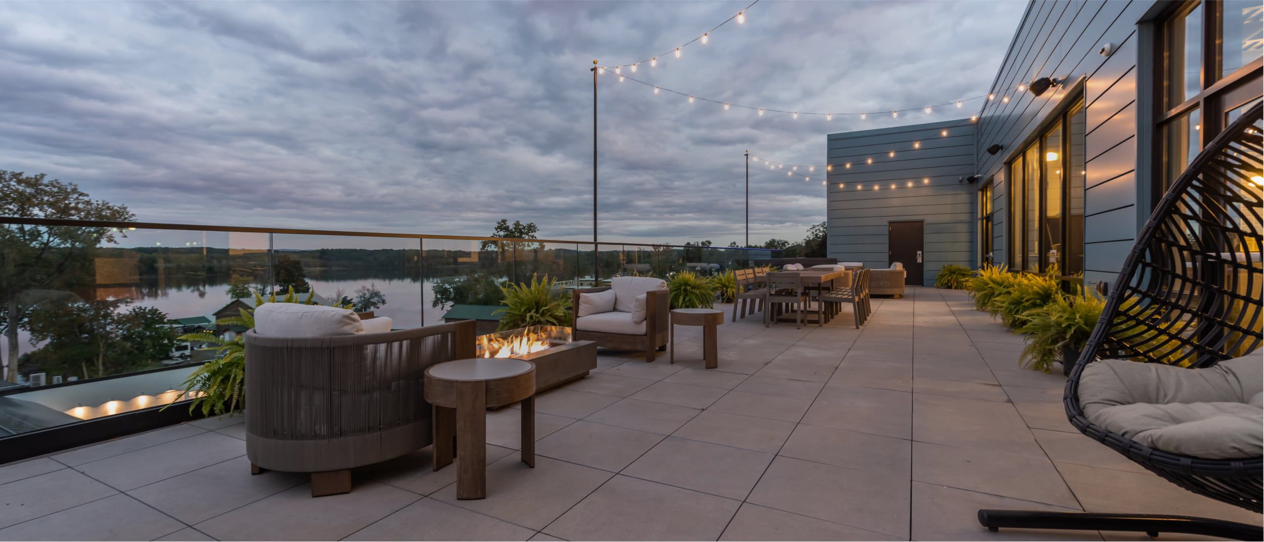 An outdoor patio overlooking the water, with a firepit and string lights setting the scene.