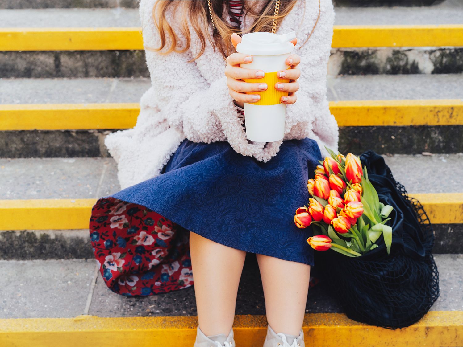 一位女士坐在台阶上，手捧咖啡，旁边放置着鲜花