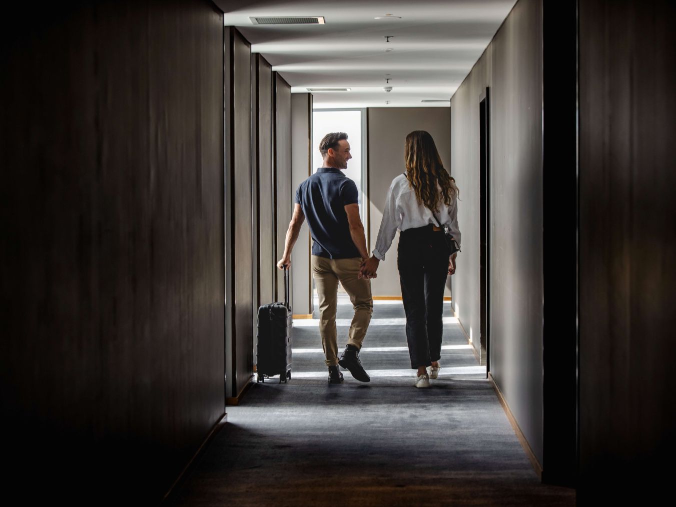 Couple walking down a hallway in a hotel with a suitcase.